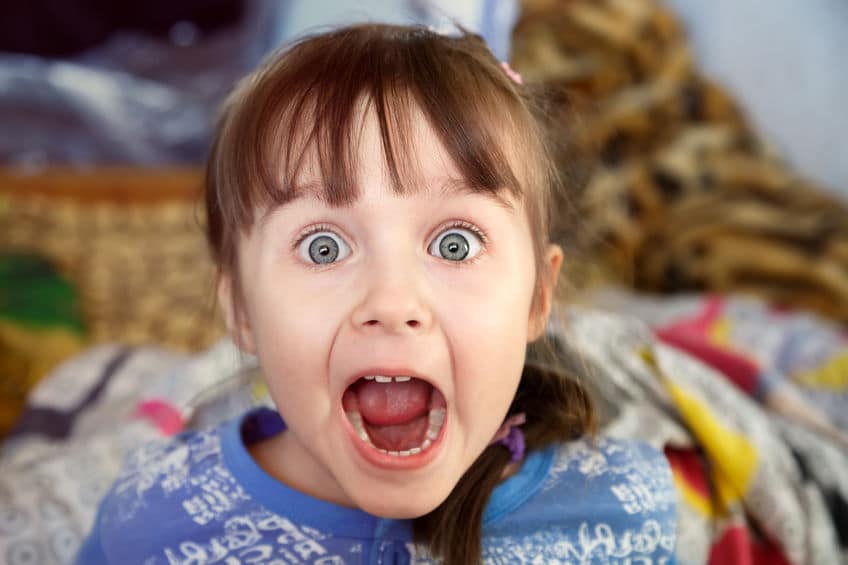 shocked screaming little girl with opened mouth in her bedroom