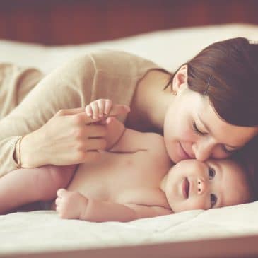 woman kissing baby on bed