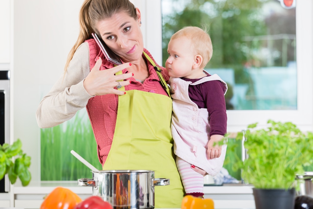 stressed mother cooking with baby and phone