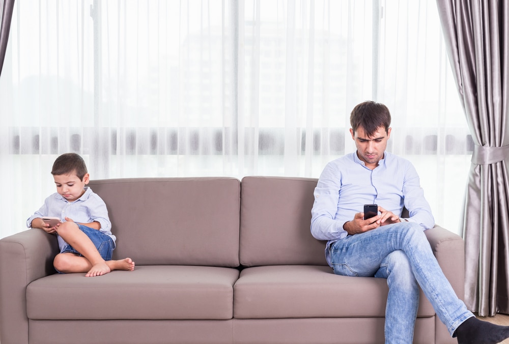 father and kid watching cellphone on couch