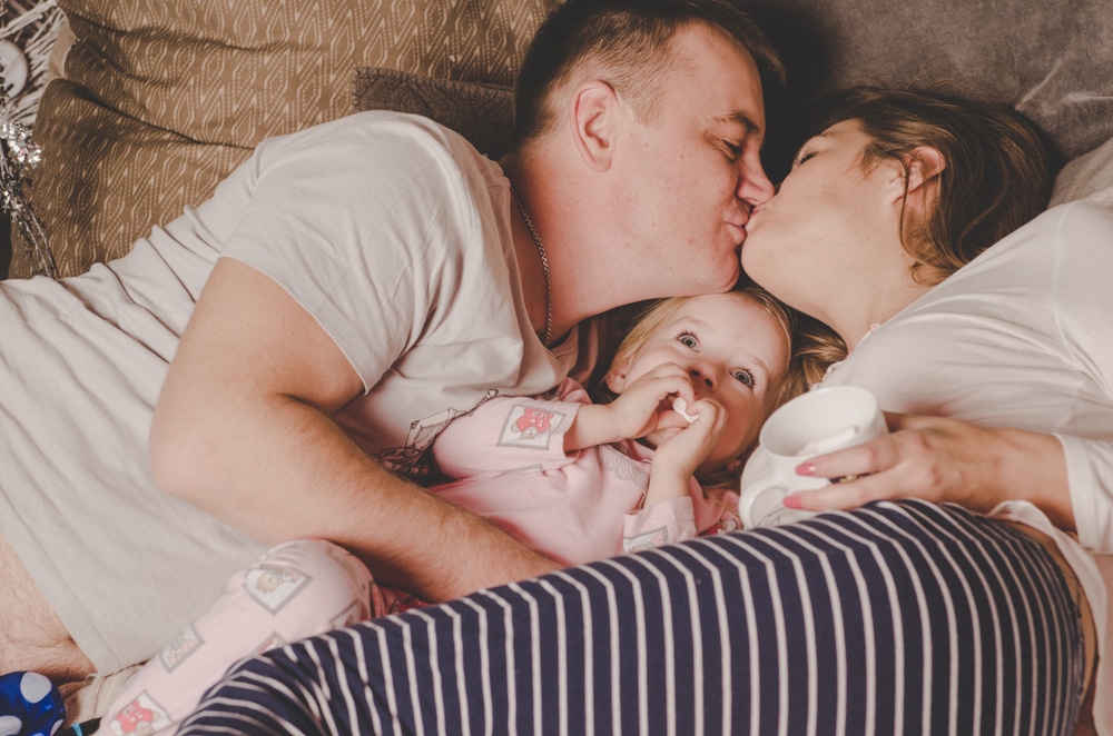 couple kissing in bed with kid