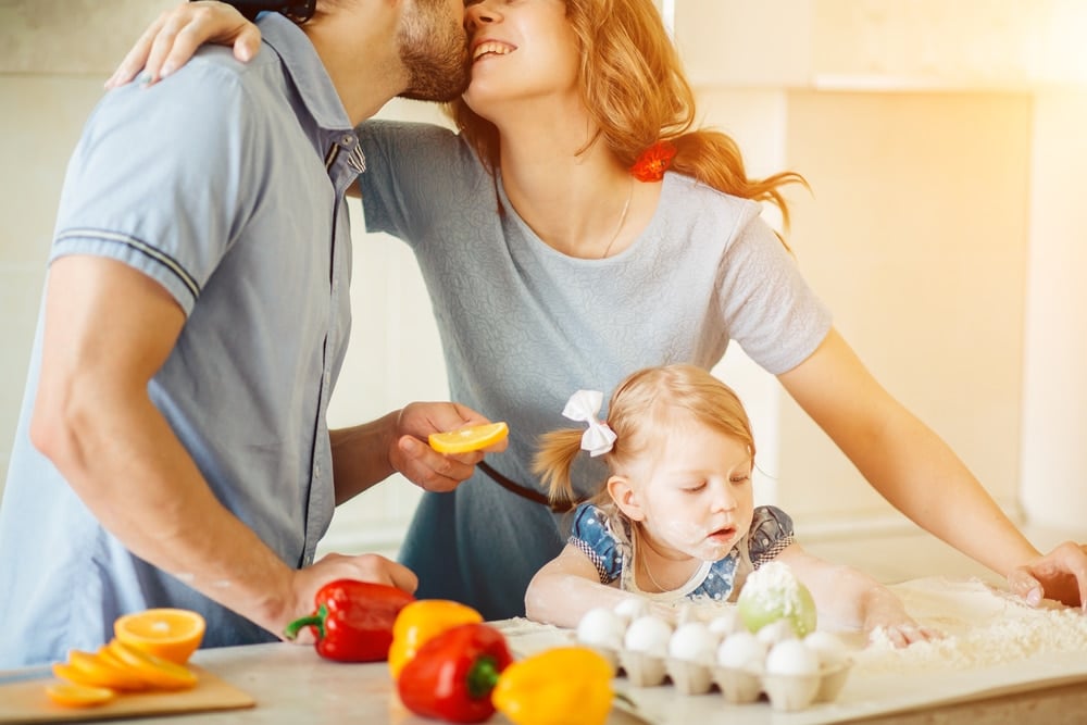 couple kissing with little girl on kitchen