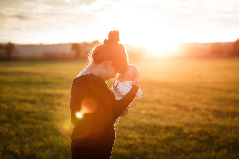 mother with newborn in a field with sun