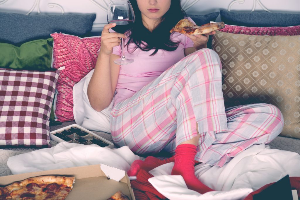 woman eating pizza and drinking wine in bed